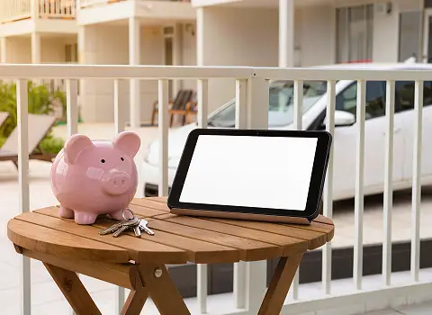 Sparschwein neben Schl&uuml;ssel und Mietwagen vor Ferienapartment