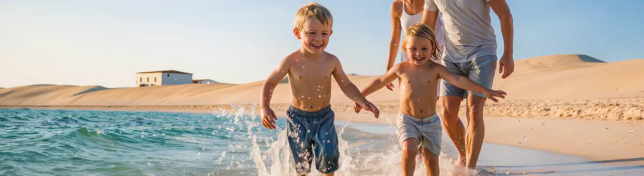 Familie mit Kindern spielt am flach abfallenden Sandstrand in Tunesien unter blauem Himmel