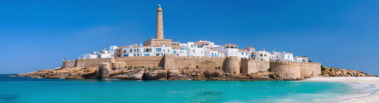 Panorama des wei&szlig;en Sandstrandes von Mahdia mit Blick auf die historische Medina und den Leuchtturm an einem klaren Tag