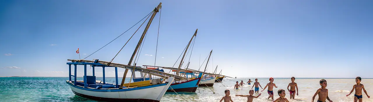 Familien mit Kindern waten im extrem flachen, tuerkisen Wasser des Strandes von Djerba.